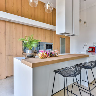 Cette image montre une grand cuisine design avec des portes de placard en bois clair, un plan de travail en surface solide, un plan de travail blanc, un évier 1 bac, un placard à porte plane, un électroménager en acier inoxydable, une péninsule et un sol gris.