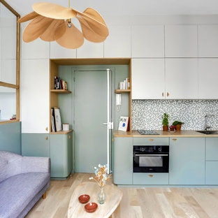 Minimalistisk inredning av ett linjärt kök med öppen planlösning, med en enkel diskho, släta luckor, träbänkskiva, flerfärgad stänkskydd, stänkskydd i mosaik, svarta vitvaror, ljust trägolv och beiget golv