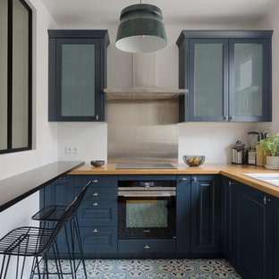 Cette image montre une cuisine design en L fermée avec un évier 3 bacs, un placard avec porte à panneau surélevé, des portes de placard bleues, un plan de travail en bois, une crédence métallisée, une crédence en ardoise, un électroménager noir, un sol multicolore et un plan de travail marron.