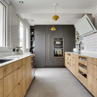 Exemple d'une cuisine tendance en U avec un évier encastré, un placard à porte plane, des portes de placard en bois clair, une crédence blanche, un électroménager encastrable, aucun îlot, un sol gris et un plan de travail blanc.
