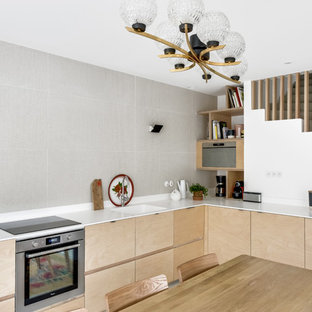 Réalisation d'une cuisine américaine design en L de taille moyenne avec un évier intégré, un placard à porte plane, des portes de placard en bois clair, un électroménager en acier inoxydable, un plan de travail en inox, une crédence blanche, un sol en bois clair et aucun îlot.
