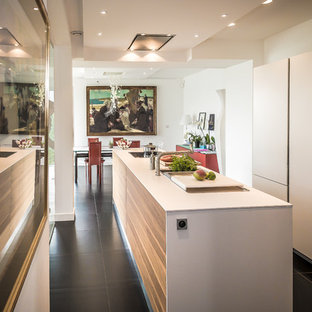 Exemple d'une cuisine américaine linéaire tendance de taille moyenne avec un îlot central, un évier intégré, des portes de placard blanches, un plan de travail en stratifié, un plan de travail blanc, un électroménager encastrable et un sol noir.