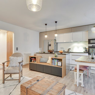 Inspiration pour une cuisine ouverte parallèle design avec un placard à porte plane, des portes de placard blanches, un électroménager en acier inoxydable, un sol en bois clair, un îlot central, un sol beige et un plan de travail gris.