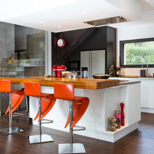 Idées déco pour une cuisine parallèle contemporaine avec un évier encastré, un placard à porte plane, des portes de placard blanches, un électroménager en acier inoxydable, un sol en bois foncé, un îlot central et un sol marron.
