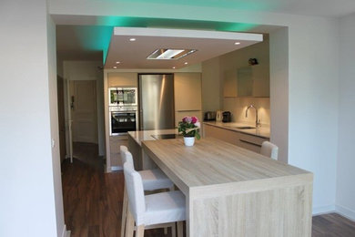 Medium sized contemporary l-shaped enclosed kitchen in Lyon with an integrated sink, beaded cabinets, beige cabinets, quartz worktops, white splashback, integrated appliances, medium hardwood flooring, an island, brown floors and white worktops.