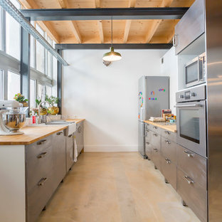Cette image montre une grand cuisine parallèle urbaine fermée avec un évier de ferme, un placard à porte plane, une façade en inox, un électroménager en acier inoxydable, aucun îlot et un plan de travail en bois.