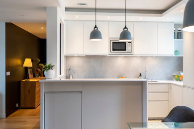 Exemple d'une petite cuisine ouverte tendance en U avec un placard à porte affleurante, une crédence grise, îlot et un plan de travail blanc.
