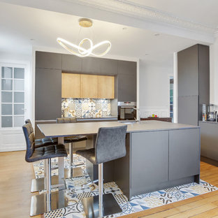 Cette photo montre une cuisine tendance avec un évier encastré, un placard à porte plane, des portes de placard grises, une crédence multicolore, un sol en bois clair, un îlot central et un plan de travail gris.