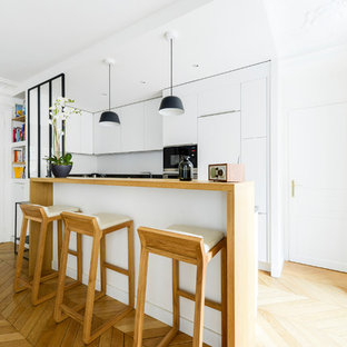 Inspiration pour une petite cuisine ouverte design en U avec un placard à porte plane, des portes de placard blanches, un plan de travail en bois, une crédence blanche, un électroménager en acier inoxydable, un sol en bois clair, une péninsule, un sol marron, un plan de travail marron et un évier encastré.