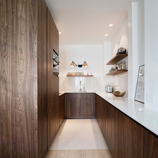 Cette photo montre une cuisine moderne en U avec un évier encastré, un placard à porte plane, des portes de placard en bois sombre, aucun îlot, un sol beige et un plan de travail blanc.