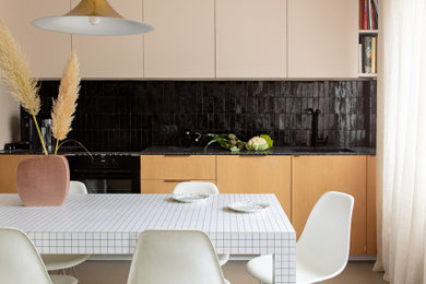 Inspiration pour une cuisine américaine linéaire minimaliste de taille moyenne avec un évier encastré, un placard à porte affleurante, un plan de travail en terrazzo, une crédence noire, un électroménager noir, sol en béton ciré, un sol gris et plan de travail noir.