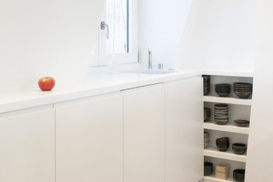 Photo of a small contemporary galley open plan kitchen in Paris with an integrated sink, beaded cabinets, white cabinets, composite countertops, white splashback, integrated appliances and ceramic flooring.