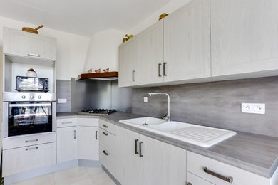 Photo of a medium sized modern l-shaped enclosed kitchen in Marseille with a single-bowl sink, beaded cabinets, grey cabinets, composite countertops, white splashback, wood splashback, stainless steel appliances, cement flooring, an island and white floors.