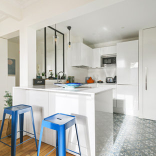 Cette photo montre une cuisine ouverte tendance en U de taille moyenne avec un évier encastré, un placard à porte affleurante, des portes de placard blanches, un plan de travail en quartz modifié, une crédence blanche, un électroménager encastrable, un sol en carreaux de ciment, un îlot central, un sol bleu et un plan de travail blanc.