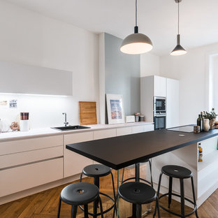 Idées déco pour une grand cuisine contemporaine avec un plan de travail en stratifié, un électroménager en acier inoxydable, un îlot central, un évier posé, un placard à porte plane, une crédence blanche, un sol en bois brun et un sol orange.