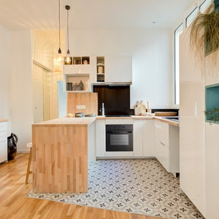 Inspiration pour une cuisine ouverte design en U de taille moyenne avec un évier encastré, des portes de placard blanches, un plan de travail en bois, une crédence noire, un électroménager encastrable, un sol en carreaux de ciment, un sol multicolore, une péninsule et un placard à porte plane.