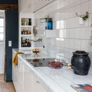 Idéer för ett mellanstort modernt vit linjärt kök med öppen planlösning, med släta luckor, vita skåp, kaklad bänkskiva, vitt stänkskydd, stänkskydd i porslinskakel, integrerade vitvaror, ljust trägolv, beiget golv och en undermonterad diskho