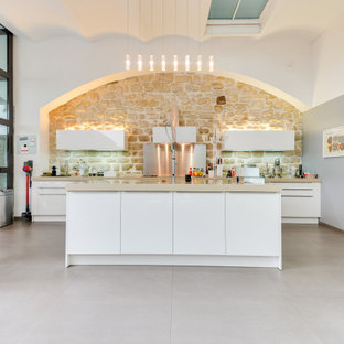 Réalisation d'une grand cuisine parallèle design avec un évier encastré, un placard à porte plane, des portes de placard blanches, un plan de travail en surface solide, une crédence beige, une crédence en carrelage de pierre, un électroménager encastrable, un sol en carrelage de porcelaine, un îlot central, un sol beige et un plan de travail beige.