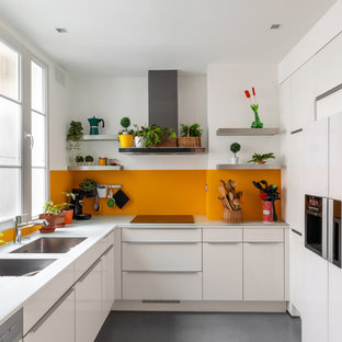 Idée de décoration pour une cuisine design en L de taille moyenne avec un évier 2 bacs, un placard à porte plane, des portes de placard blanches, un plan de travail en verre, un électroménager encastrable, un sol en carrelage de céramique, aucun îlot, un sol gris, un plan de travail blanc, une crédence orange et une crédence en feuille de verre.