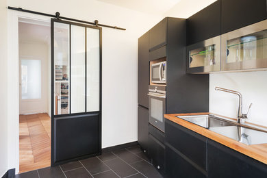 Example of a mid-sized trendy single-wall ceramic tile and black floor enclosed kitchen design in Paris with an undermount sink, black cabinets, wood countertops, paneled appliances and no island