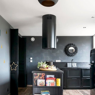 Aménagement d'une cuisine contemporaine en L fermée et de taille moyenne avec des portes de placard noires, une crédence noire, un électroménager noir, un sol en bois clair et une péninsule.
