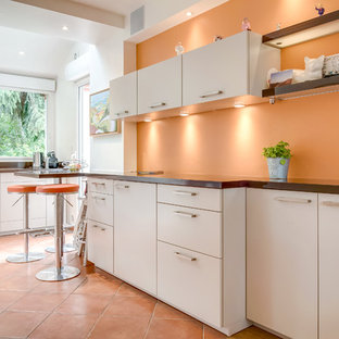 Aménagement d'une cuisine contemporaine avec un placard à porte plane, une crédence orange, un sol en carreau de terre cuite, une péninsule, un sol orange, un plan de travail marron, un électroménager en acier inoxydable, un évier 2 bacs, des portes de placard beiges et un plan de travail en bois.