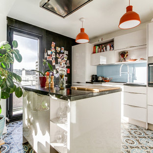 Cette image montre une cuisine nordique avec un placard à porte plane, des portes de placard blanches, une crédence bleue, une crédence en feuille de verre, un îlot central, un sol multicolore et un plan de travail noir.