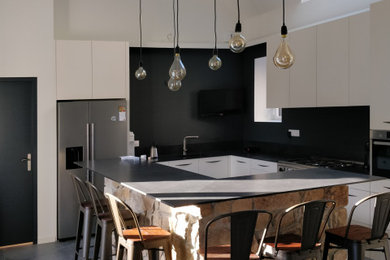 Exemple d'une grande cuisine ouverte industrielle en L avec un évier encastré, un placard à porte affleurante, un électroménager en acier inoxydable, un sol en carrelage de céramique, îlot, un sol gris et plan de travail noir.