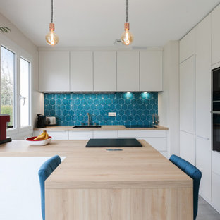 Aménagement d'une grand cuisine ouverte parallèle contemporaine avec un îlot central, un placard à porte plane, des portes de placard blanches, un évier encastré, un plan de travail en bois, une crédence bleue, une crédence en mosaïque, un électroménager encastrable, sol en stratifié, un sol gris et un plan de travail marron.