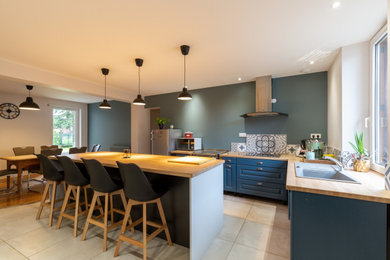 Idée de décoration pour une cuisine ouverte parallèle tradition de taille moyenne avec un évier encastré, un plan de travail en bois, une crédence en carreau de ciment, un électroménager en acier inoxydable, un sol en carrelage de céramique, îlot et un sol beige.