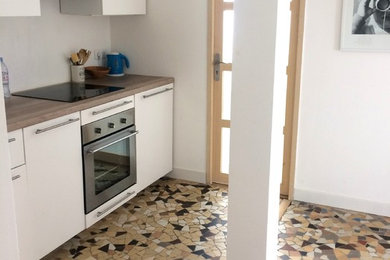 パリにあるお手頃価格の小さなコンテンポラリースタイルのおしゃれなキッチン (シングルシンク、フラットパネル扉のキャビネット、白いキャビネット、木材カウンター、白いキッチンパネル、パネルと同色の調理設備、セラミックタイルの床、アイランドなし、ベージュの床、ベージュのキッチンカウンター) の写真