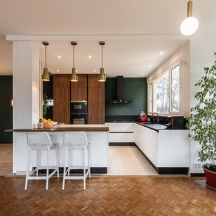 Cette photo montre une cuisine ouverte tendance en L de taille moyenne avec un évier encastré, un plan de travail en surface solide, une crédence noire, un sol en carrelage de céramique, un sol beige, un plan de travail noir, un placard à porte plane, des portes de placard en bois sombre, un électroménager noir et une péninsule.