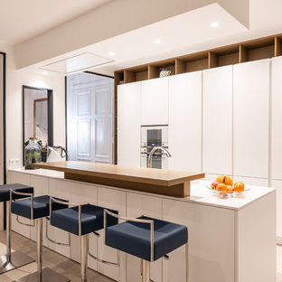 Idées déco pour une cuisine contemporaine avec un placard à porte plane, des portes de placard blanches, un électroménager blanc, un îlot central, un sol beige et un plan de travail blanc.