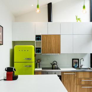 Aménagement d'une petit cuisine ouverte contemporaine en L avec une crédence blanche, un îlot central, un évier 1 bac, un placard avec porte à panneau encastré, des portes de placard en bois clair, un plan de travail en stratifié, une crédence en carreau de verre, un électroménager encastrable, un sol en bois peint, un sol blanc et un plan de travail blanc.