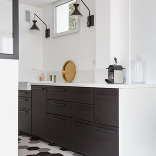 Cette image montre une petit cuisine ouverte parallèle design avec un évier de ferme, un placard à porte plane, un sol multicolore, un plan de travail blanc, des portes de placard noires, un plan de travail en quartz, une crédence blanche, une crédence en dalle de pierre, un électroménager noir, un sol en carrelage de céramique et aucun îlot.