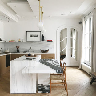 Exemple d'une cuisine tendance en L avec des portes de placard en bois clair, une crédence blanche, une crédence en dalle de pierre, un sol en bois clair, un îlot central, un sol beige et un plan de travail blanc.