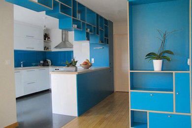 Cette photo montre une cuisine moderne de taille moyenne avec un placard à porte plane, des portes de placard blanches, un plan de travail en stratifié, une crédence bleue, une crédence en feuille de verre et un sol gris.