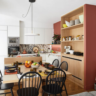 Idées déco pour une cuisine américaine contemporaine en L de taille moyenne avec un évier posé, un placard à porte plane, des portes de placard blanches, une crédence grise, un électroménager encastrable, un îlot central, un sol marron et un plan de travail gris.