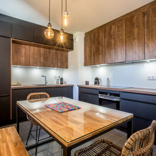 Réalisation d'une cuisine design en L fermée avec un évier posé, un placard à porte plane, des portes de placard noires, un plan de travail en bois, une crédence en feuille de verre, un électroménager encastrable, aucun îlot, un sol marron et un plan de travail marron.
