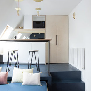 Design ideas for a small contemporary galley open plan kitchen in Paris with a single-bowl sink, flat-panel cabinets, light wood cabinets, wood benchtops, black splashback, glass sheet splashback, black appliances, concrete floors, a peninsula and blue floor.