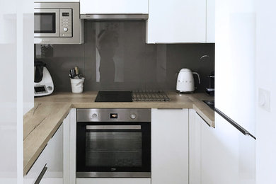 Exempel på ett litet minimalistiskt beige beige kök, med en enkel diskho, luckor med profilerade fronter, vita skåp, träbänkskiva, grått stänkskydd, glaspanel som stänkskydd, rostfria vitvaror, vinylgolv och grått golv