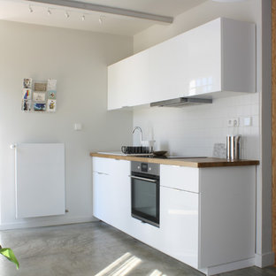 Inspiration pour une cuisine linéaire design avec un évier posé, un placard à porte plane, des portes de placard blanches, un plan de travail en bois, une crédence blanche, béton au sol, un sol gris et un plan de travail marron.