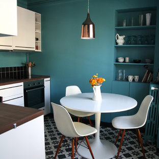 Réalisation d'une petit cuisine américaine design en L avec un placard à porte plane, des portes de placard blanches, un plan de travail en bois, une crédence noire, un électroménager en acier inoxydable, aucun îlot et un sol en carrelage de céramique.