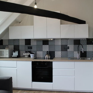 Exemple d'une cuisine ouverte linéaire tendance de taille moyenne avec un évier posé, des portes de placard blanches, un plan de travail en bois, une crédence multicolore, une crédence en carreau de ciment, un électroménager encastrable, un sol en bois clair et aucun îlot.