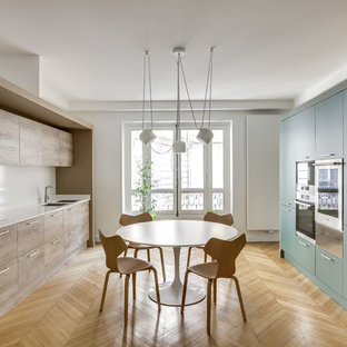 Réalisation d'une cuisine parallèle design fermée avec un évier encastré, un placard à porte plane, des portes de placards vertess, une crédence blanche, un électroménager noir, un sol en bois clair, aucun îlot, un sol beige et un plan de travail blanc.