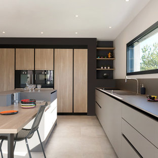 Cette photo montre une cuisine américaine tendance avec des portes de placard grises, un plan de travail en surface solide, une crédence grise, un électroménager noir, un sol en carrelage de céramique, un îlot central, un sol gris, un plan de travail gris, un évier 2 bacs et un placard à porte plane.