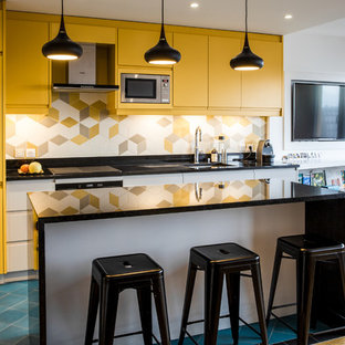 Idée de décoration pour une cuisine ouverte nordique de taille moyenne avec des portes de placard jaunes, une crédence en carreau de porcelaine, un électroménager en acier inoxydable, un sol en carrelage de céramique, un îlot central, un sol bleu, un plan de travail noir, un évier encastré, un placard à porte plane et une crédence multicolore.