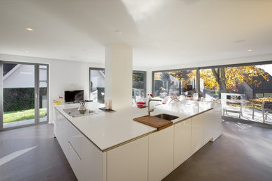 Cette image montre une cuisine design avec un évier 1 bac, un placard à porte affleurante, des portes de placard blanches, un électroménager en acier inoxydable, sol en béton ciré, un sol gris et un plan de travail blanc.