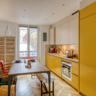 Réalisation d'une cuisine américaine linéaire design avec un évier 1 bac, un placard à porte plane, des portes de placard jaunes, une crédence beige, un électroménager en acier inoxydable, un sol en bois clair, aucun îlot, un sol beige et un plan de travail beige.