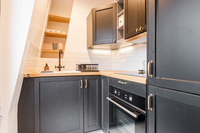 Inspiration pour une cuisine américaine design en L de taille moyenne avec un évier encastré, un placard à porte plane, des portes de placard noires, un plan de travail en bois, une crédence blanche, une crédence en céramique, un électroménager noir, un sol en carrelage de céramique, un sol blanc et un plan de travail beige.